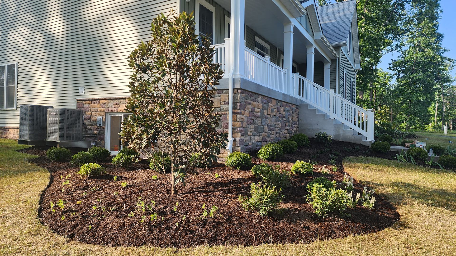 House with brown mulch flower bed, tree, and green bushes.