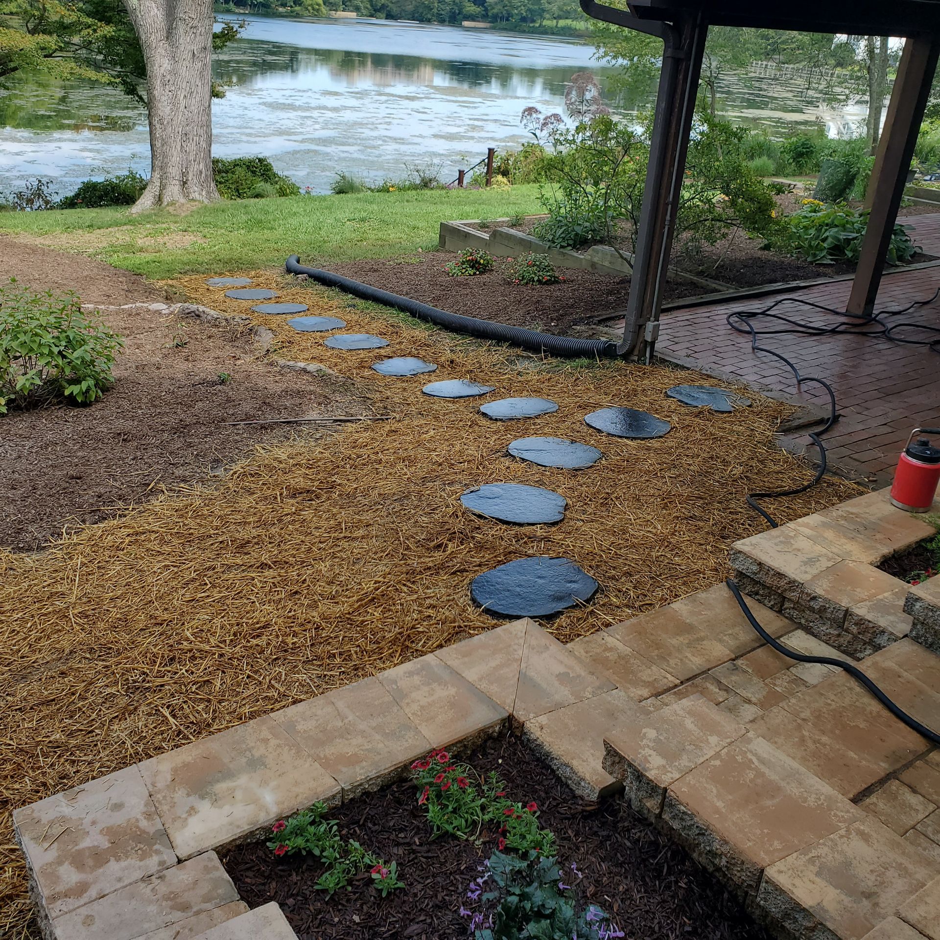 Stone path with stepping stones leads to a waterfront, near a patio with flower beds.