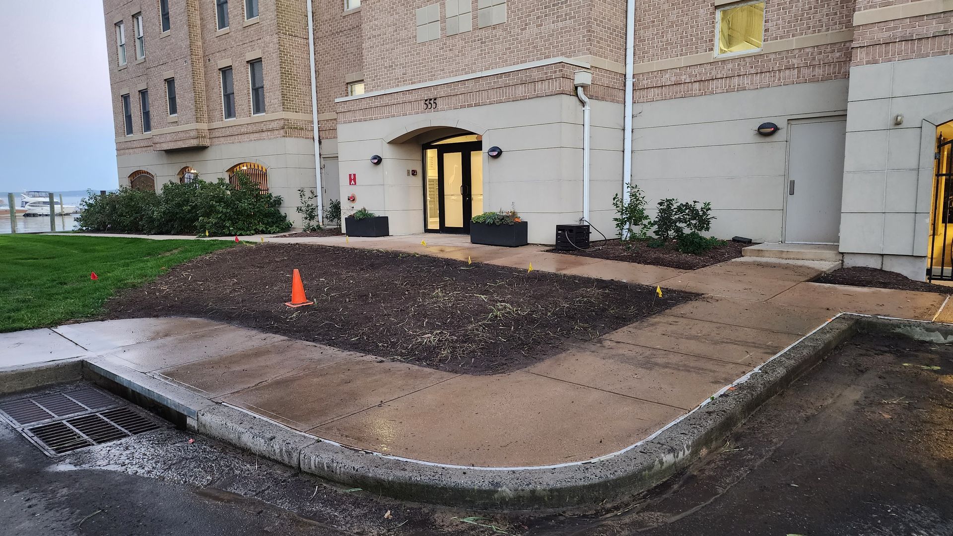 Exterior of a building with a walkway and newly planted flower bed. Orange cone present.