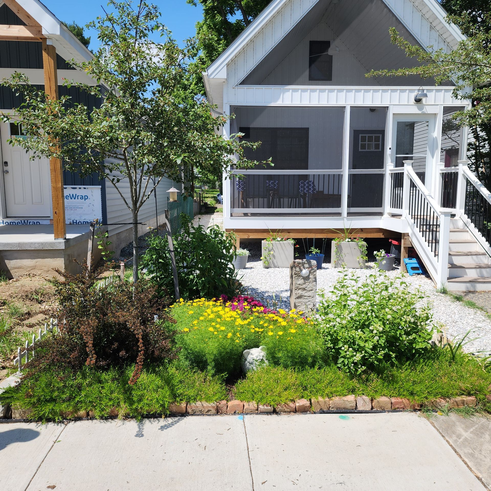 Small white house with a screened porch, front garden with flowers, and brick border along a sidewalk.