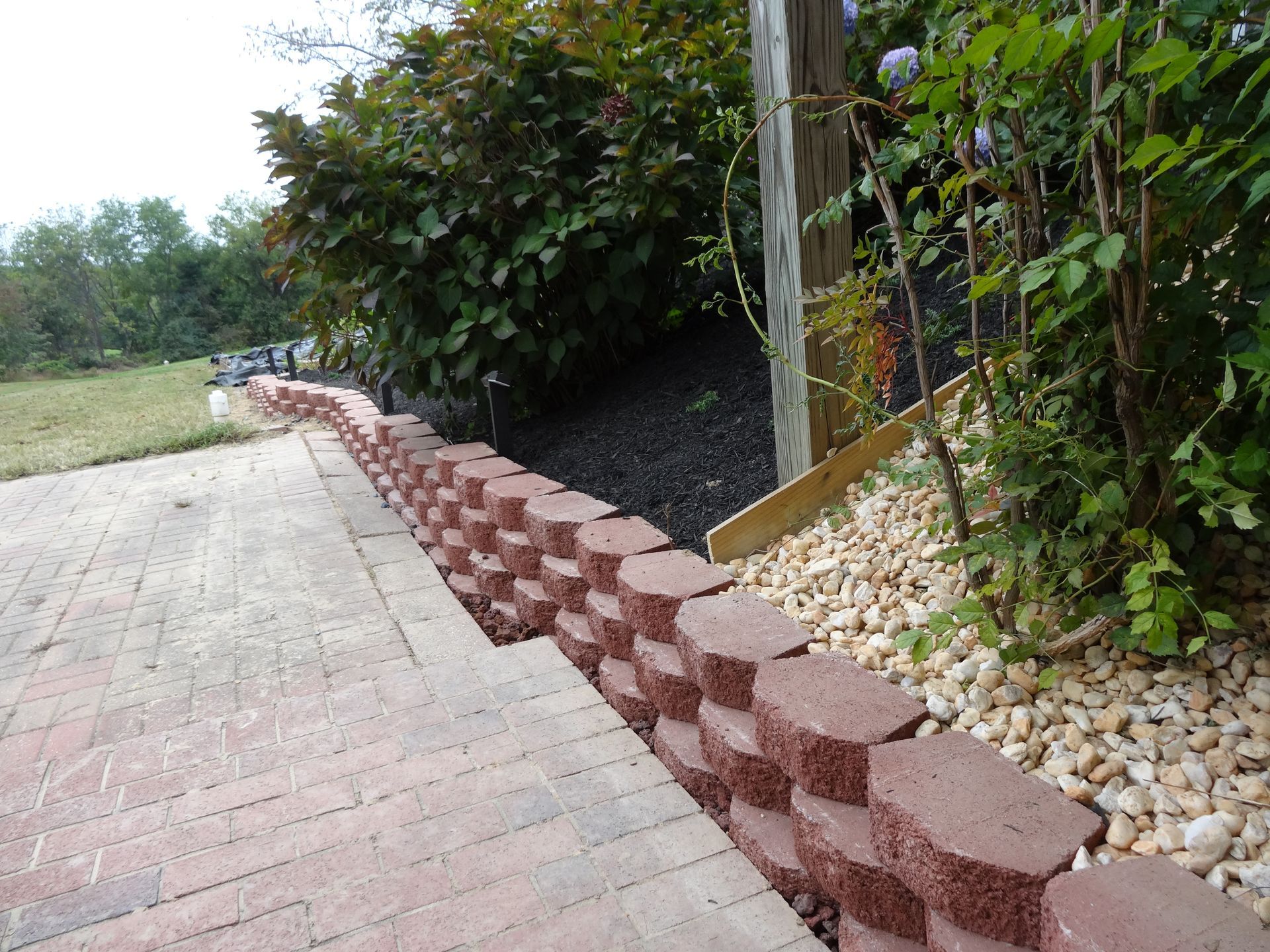 Red brick retaining wall alongside a brick path and gravel garden bed with bushes.