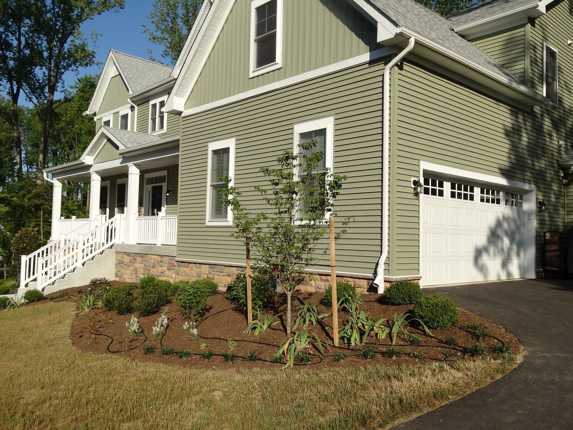 Two-story green house with white trim, garage, landscaping and driveway.