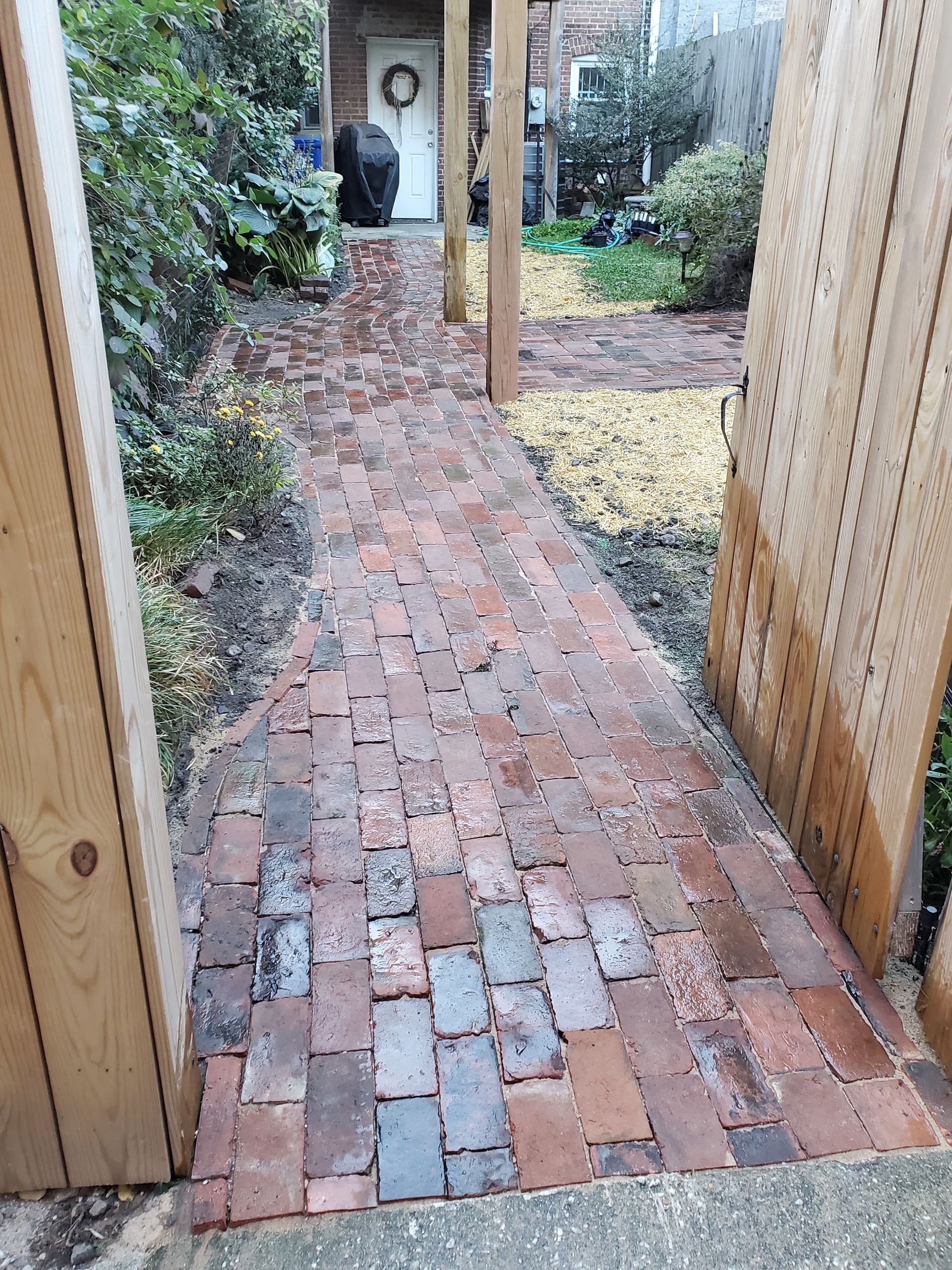 Brick pathway leading to a white door, framed by wooden posts and greenery.