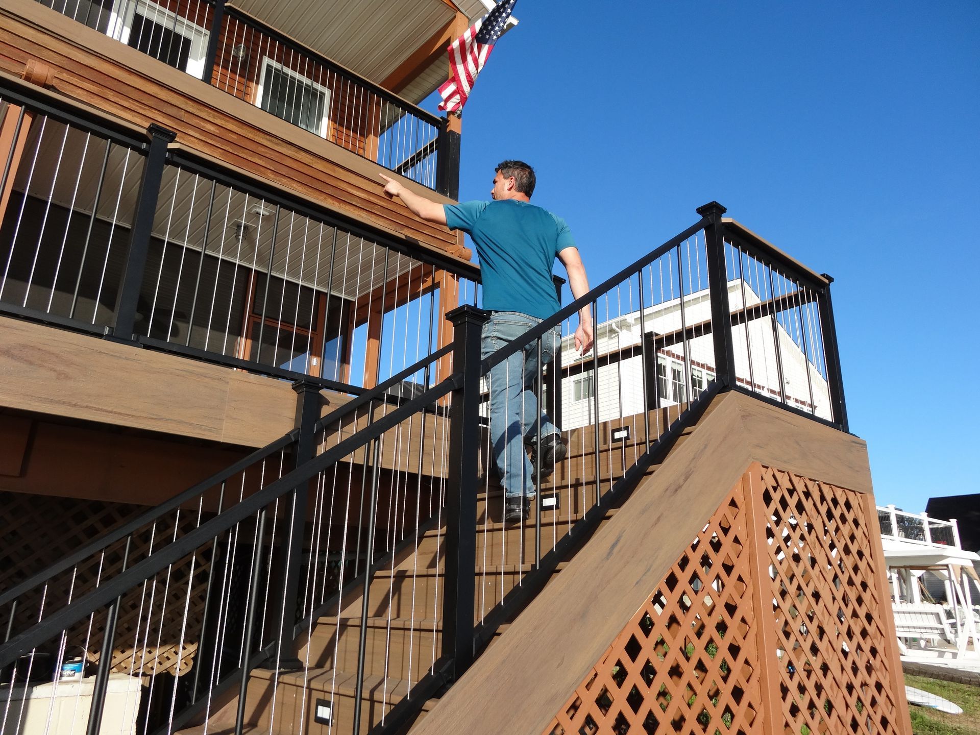 Man ascends wooden stairs towards a deck, reaching for an American flag. Sunny day.