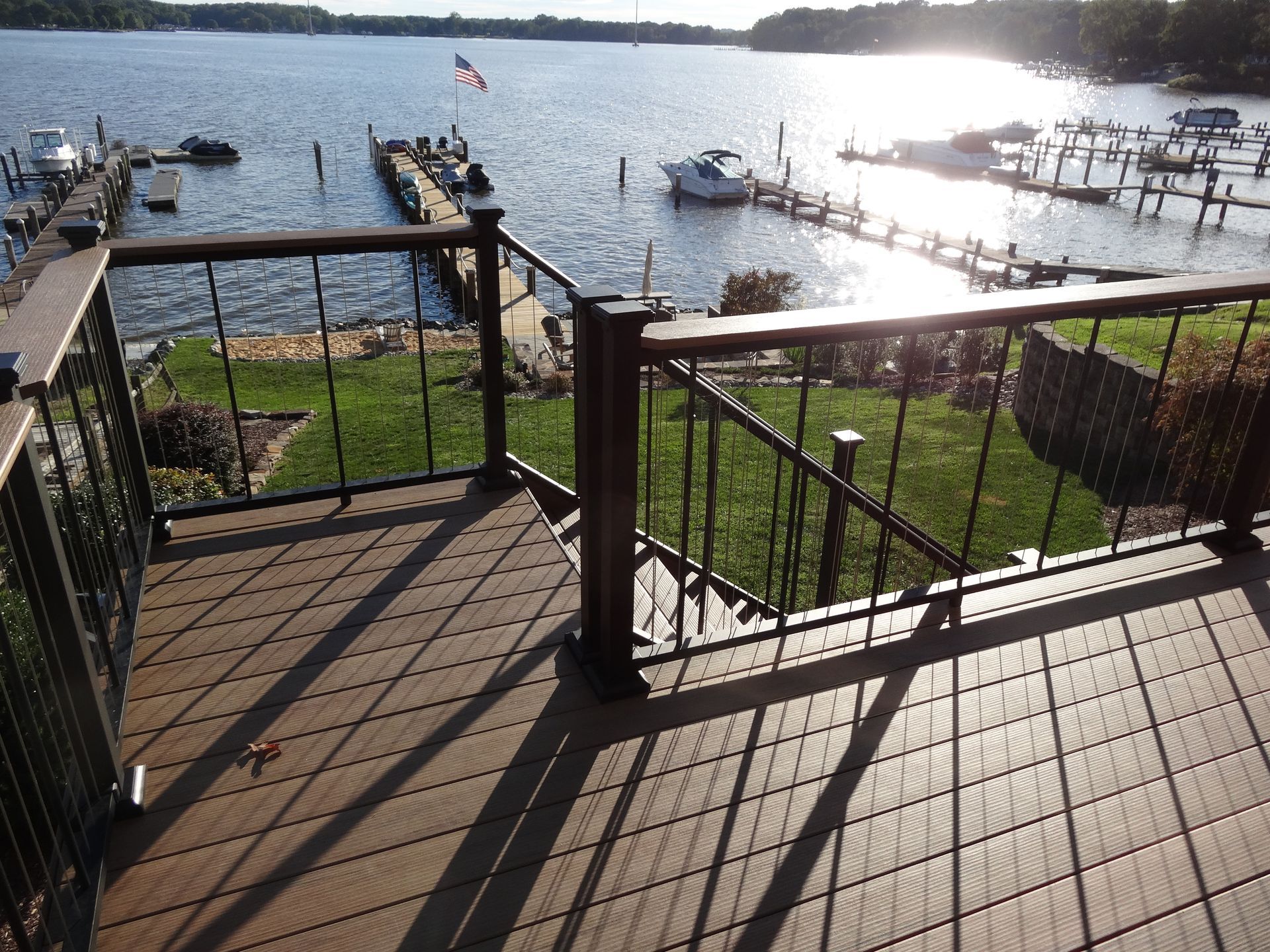 Deck overlooking a lake with docks and boats. Brown deck, black railing, and green grass.
