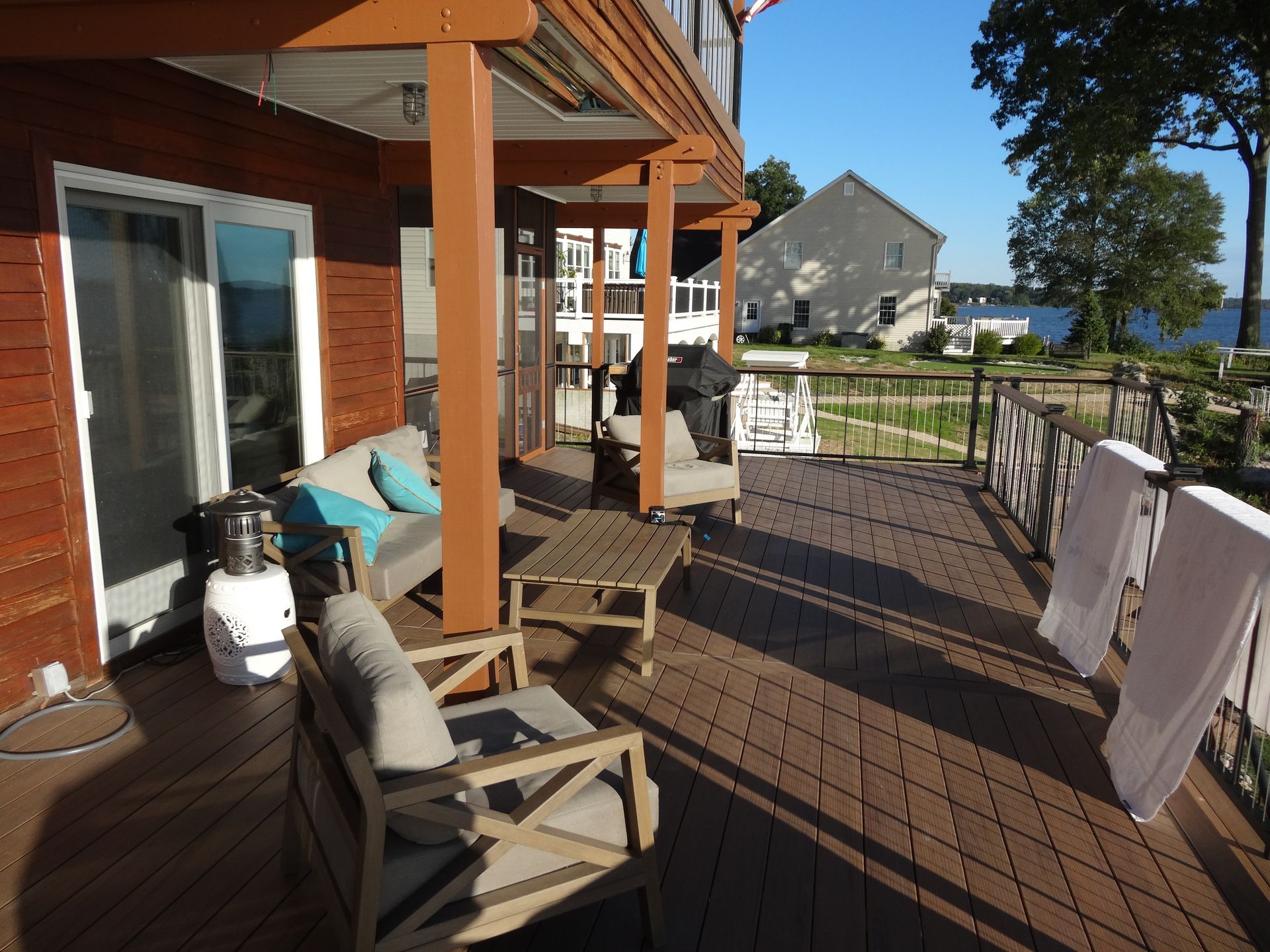 Wooden deck with outdoor furniture, overlooking water and houses.