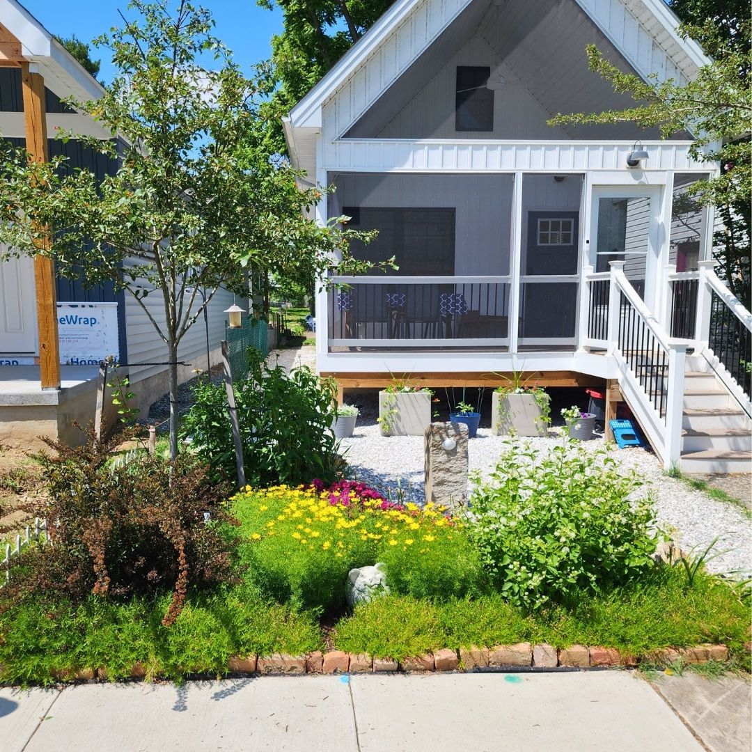 Small white house with a porch and a colorful flower garden in front.
