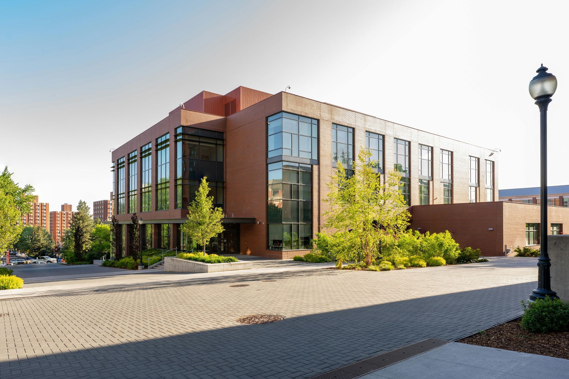 Brick building with large windows, trees, and a paved walkway under a sunny sky.