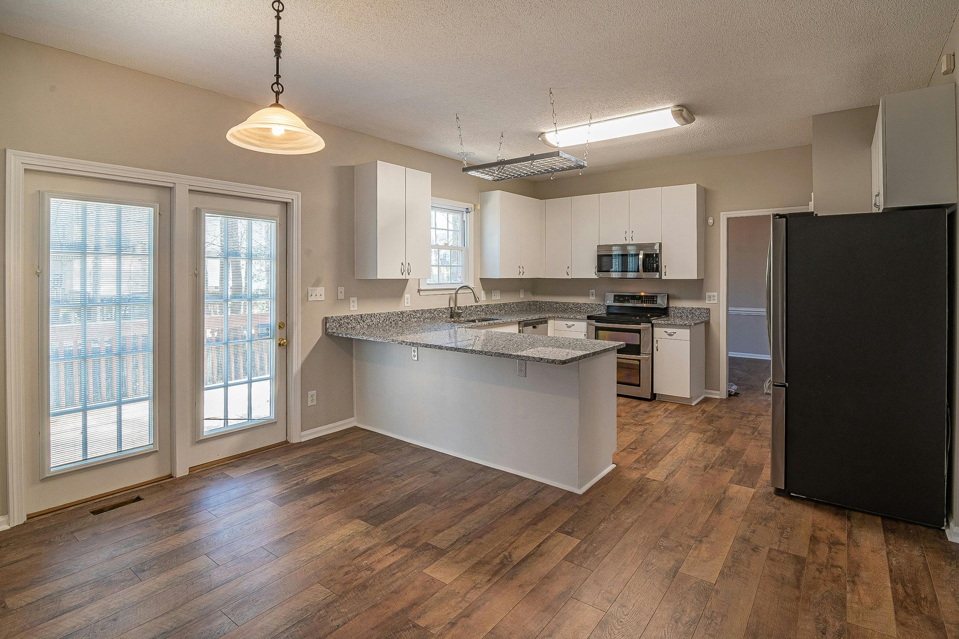 A kitchen with hardwood floors , white cabinets , stainless steel appliances and a black refrigerator.