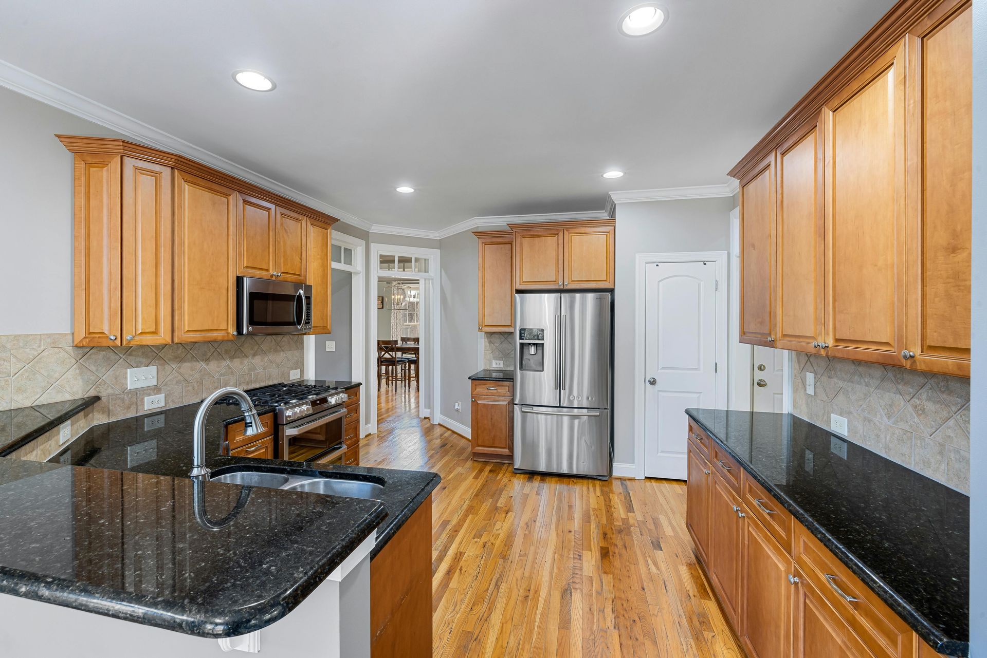 A kitchen with stainless steel appliances , granite counter tops , wooden cabinets and hardwood floors.