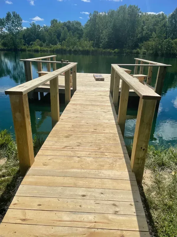 A wooden dock leading to a lake with trees in the background.