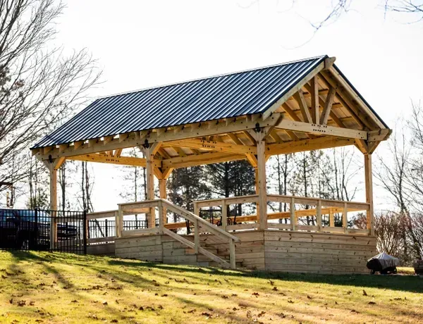 A wooden pavilion with a metal roof is sitting on top of a lush green field. A wooden pavilion with a metal roof is sitting on top of a lush green field.