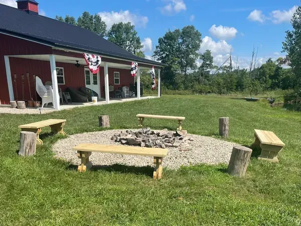 A fire pit with benches around it in front of a red barn.