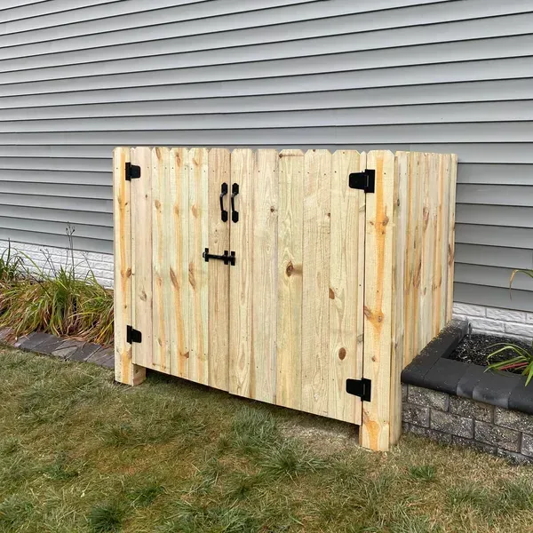 A wooden trash can is sitting in the grass next to a house.