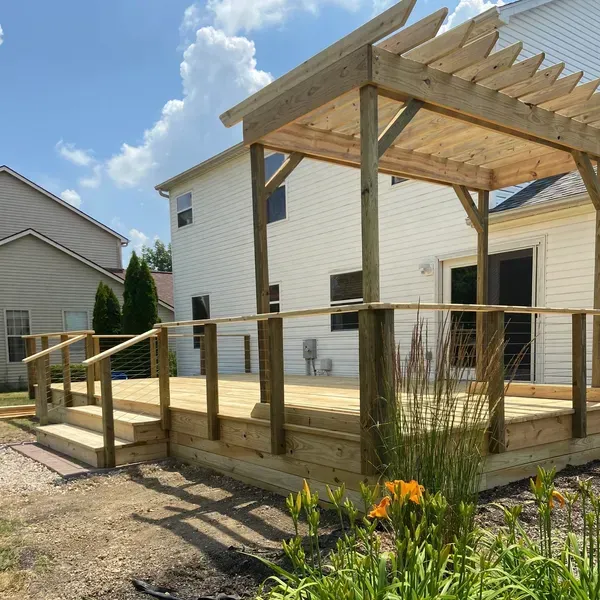 A wooden deck with a pergola in front of a white house