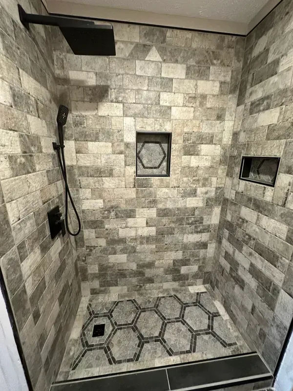 A shower with a brick wall and a black shower head.