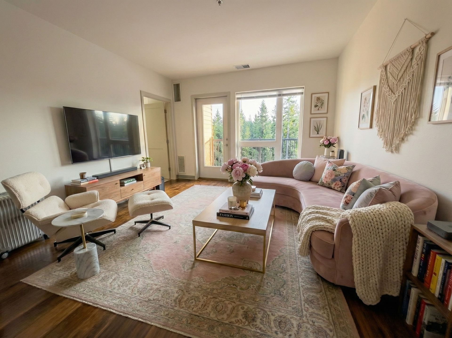 Cozy living room with pink sofa, white chair, TV, rug, and large windows with trees outside.