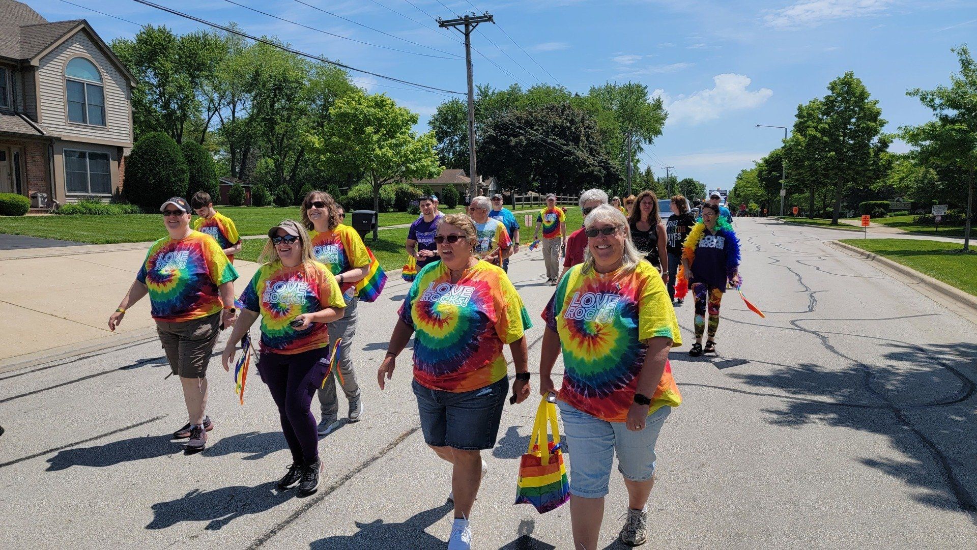 A group of people are walking down a street wearing tie dye shirts.