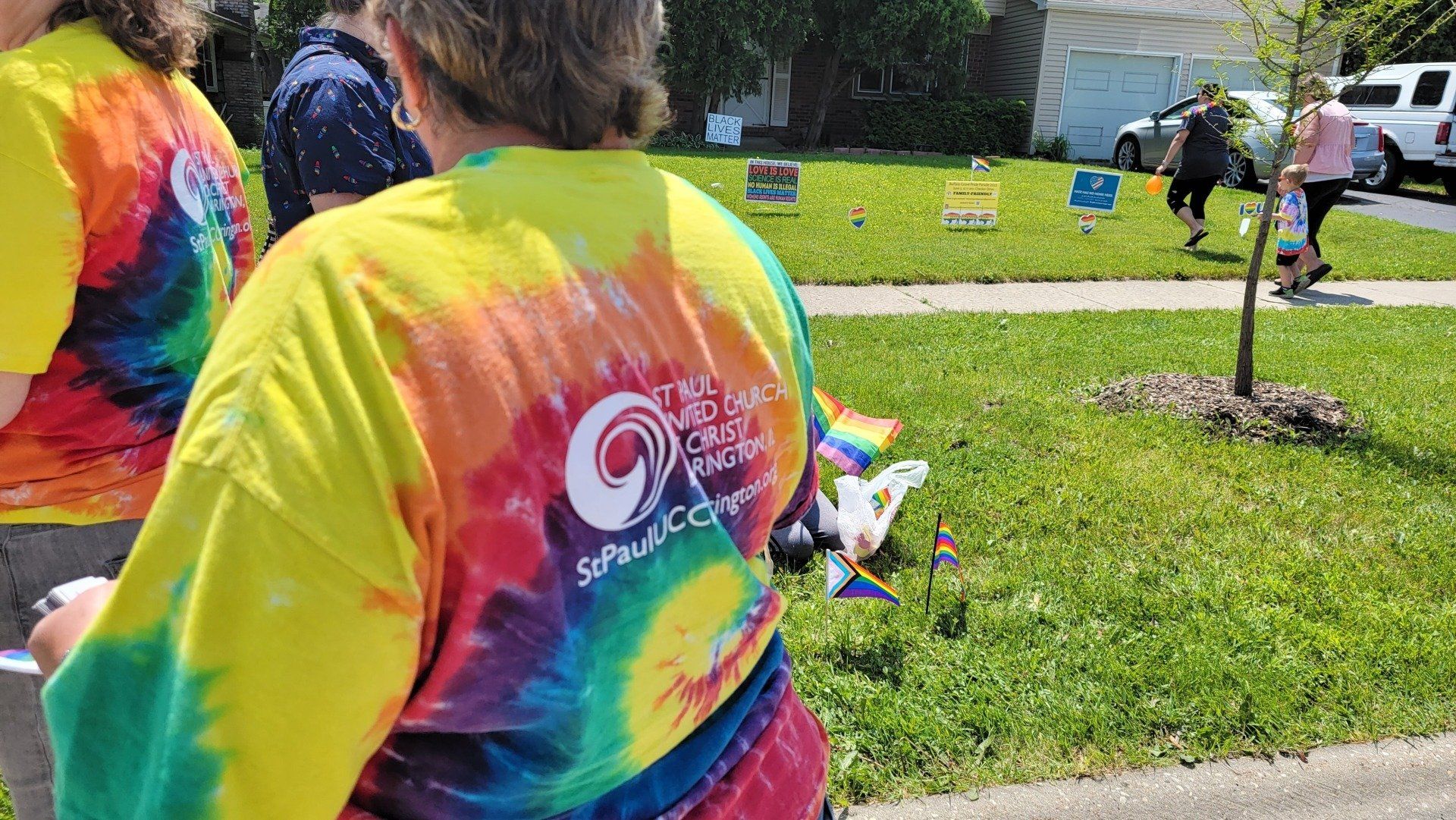 A person wearing a tie dye shirt is standing in the grass.