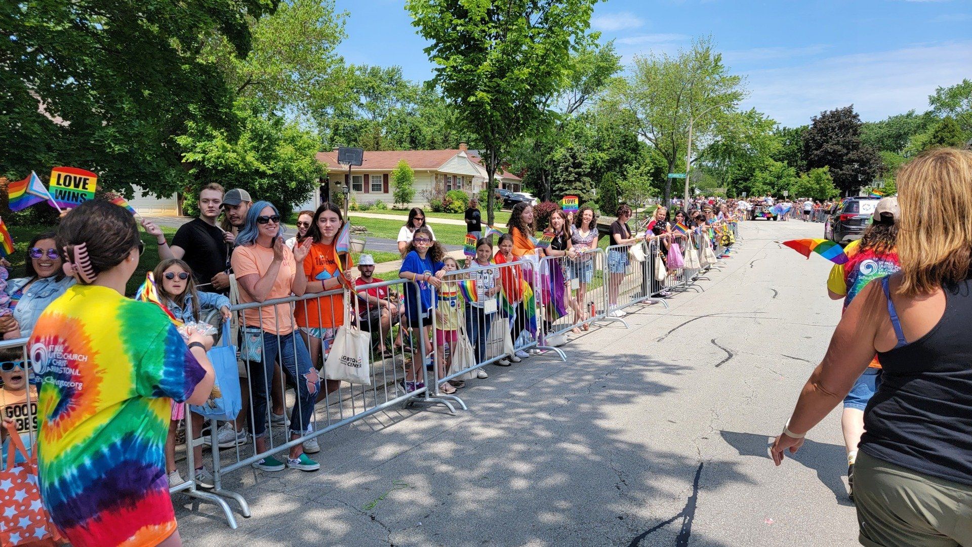 A woman in a tie dye shirt is standing in front of a crowd of people watching a parade.