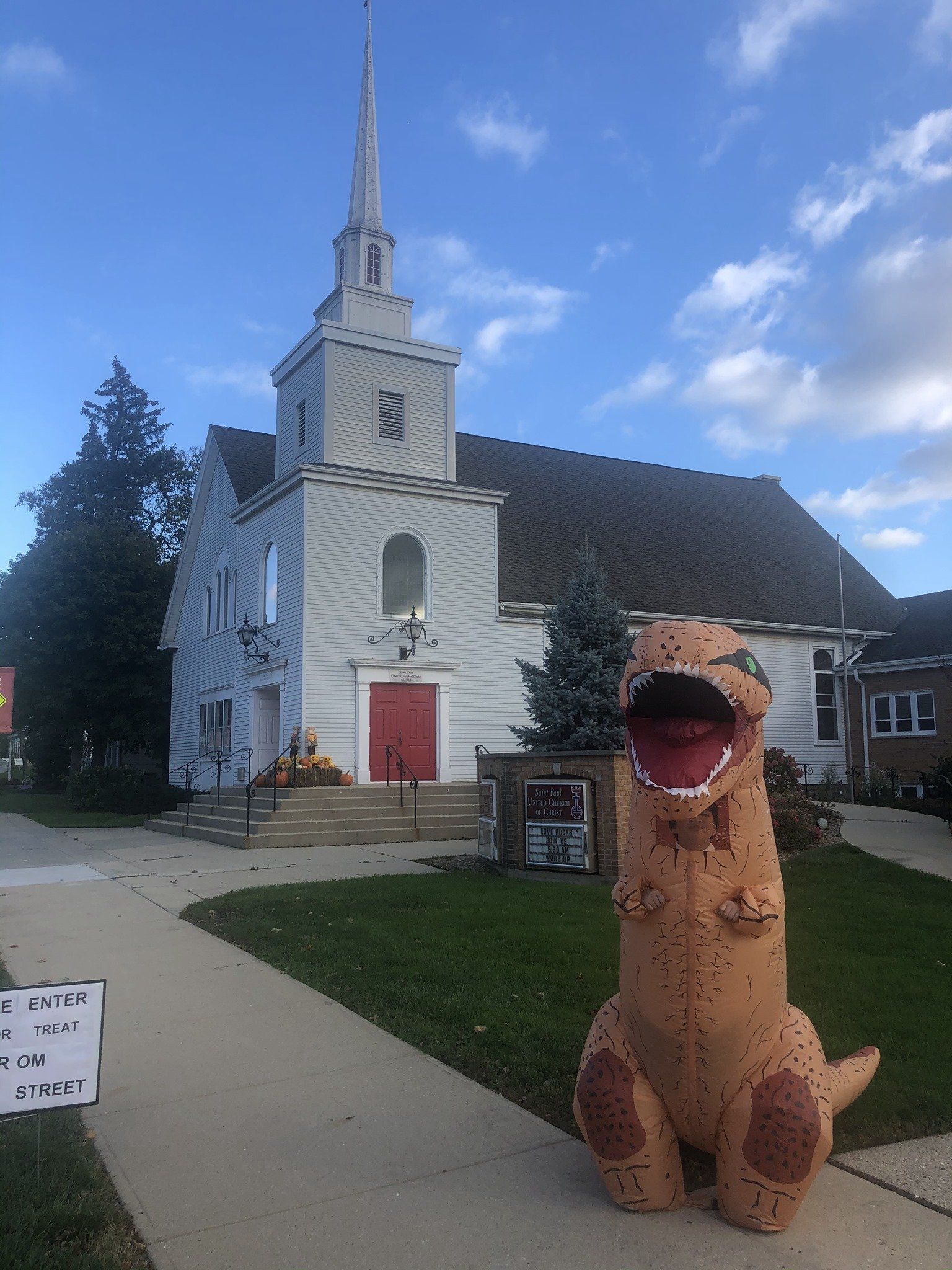 A stuffed dinosaur is standing in front of a church