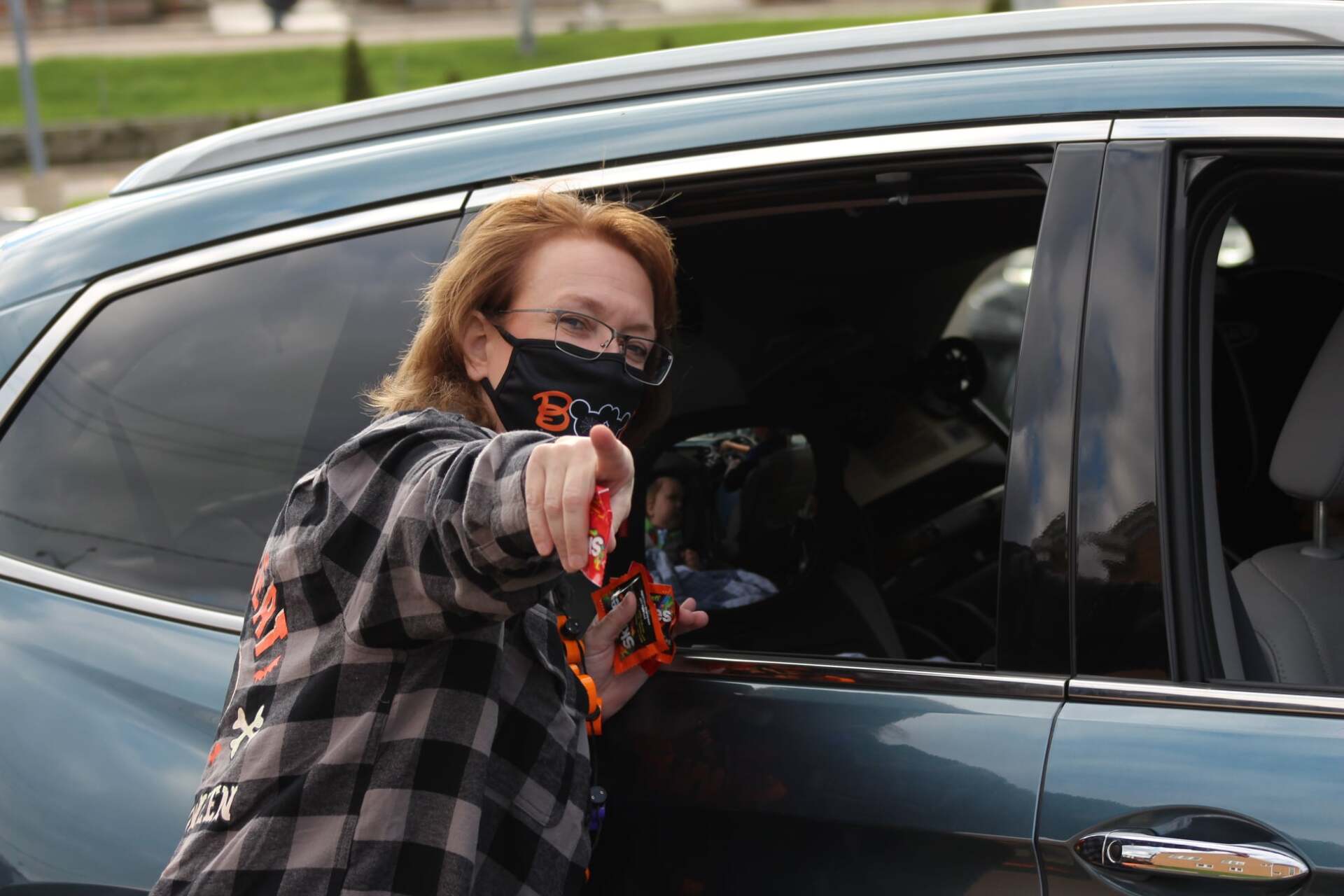 A woman wearing a mask is pointing out the window of a car.