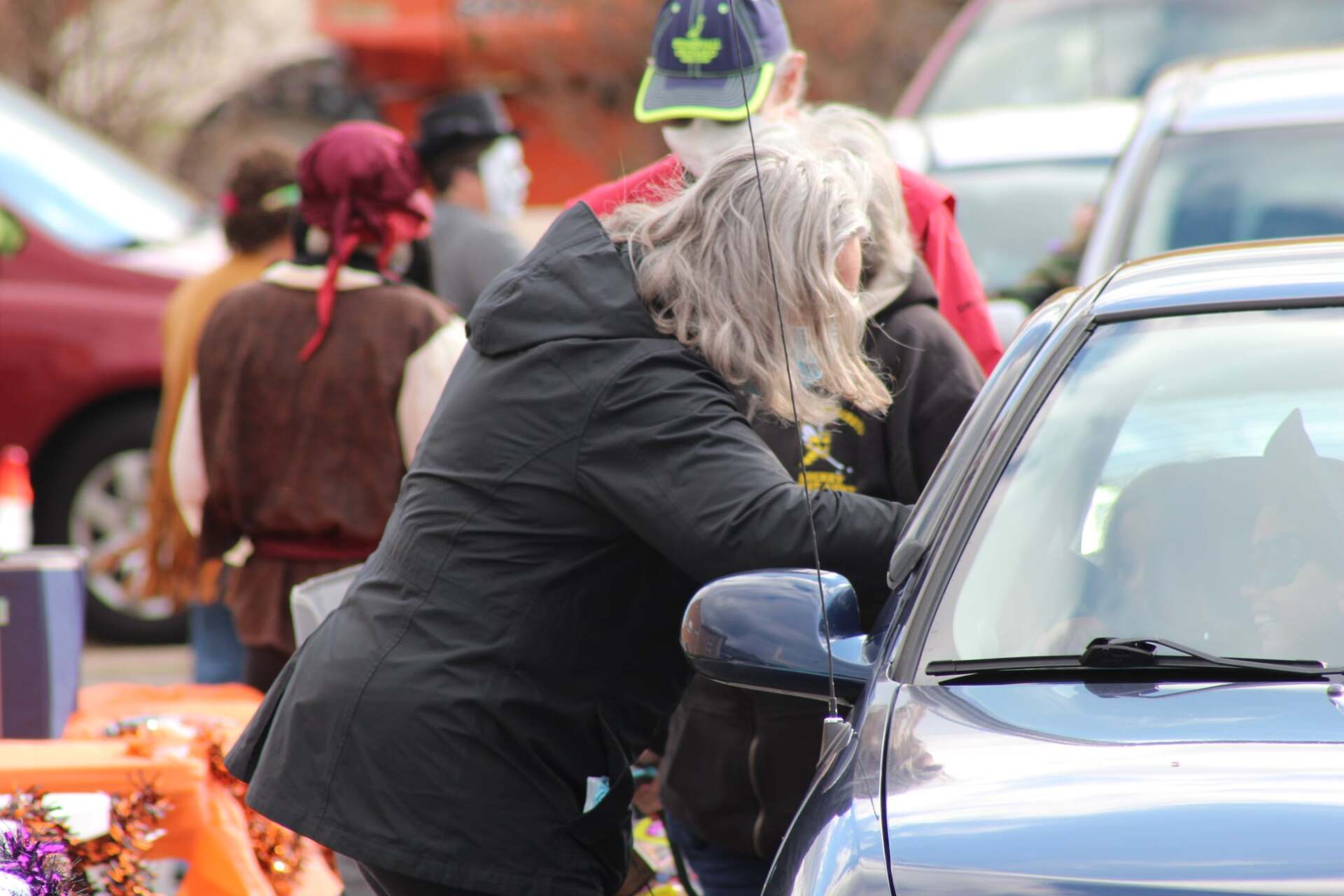 A woman is standing next to a blue car in a parking lot.