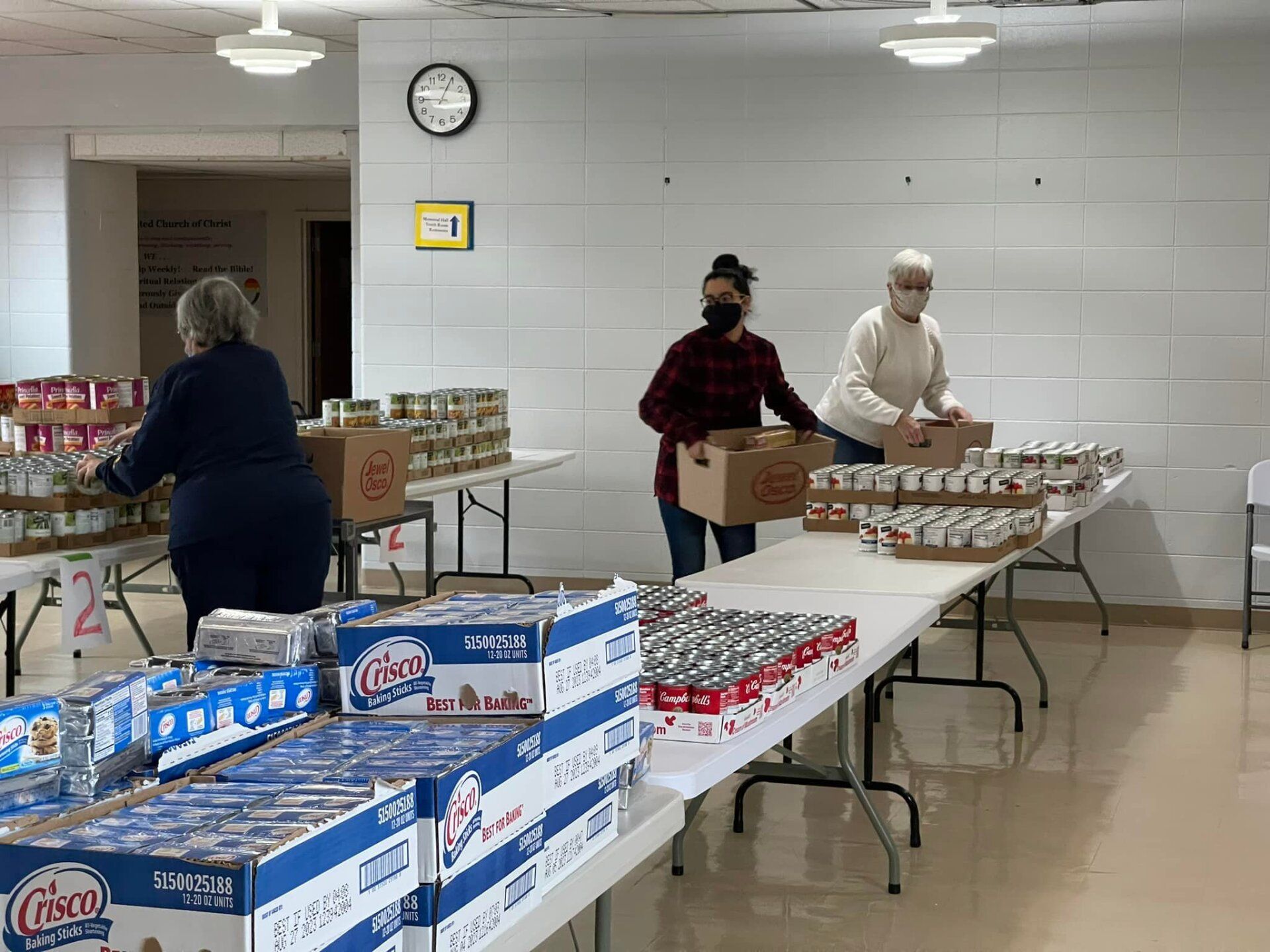 A group of people are standing around tables filled with canned goods.