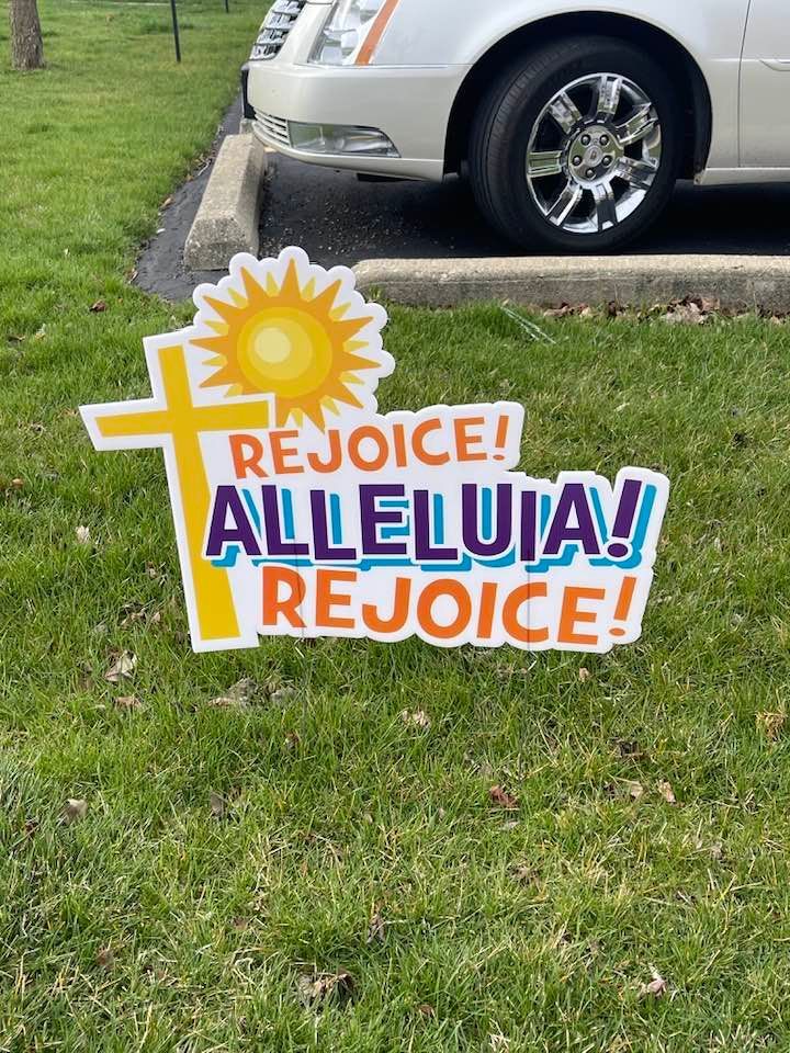 A white car is parked next to a sign that says rejoice ! alleluia ! rejoice !