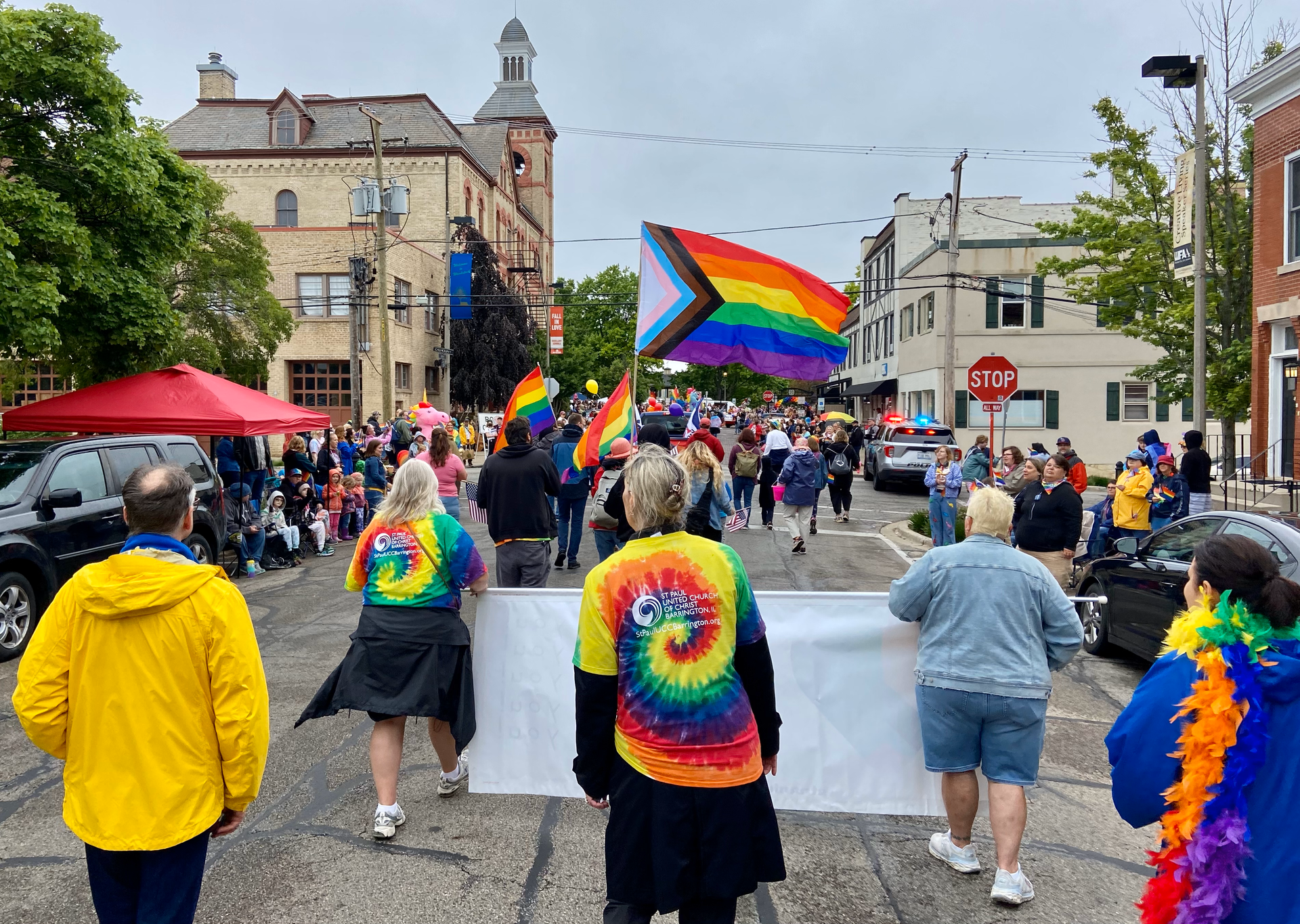 A group of people are walking down a street holding a rainbow flag.