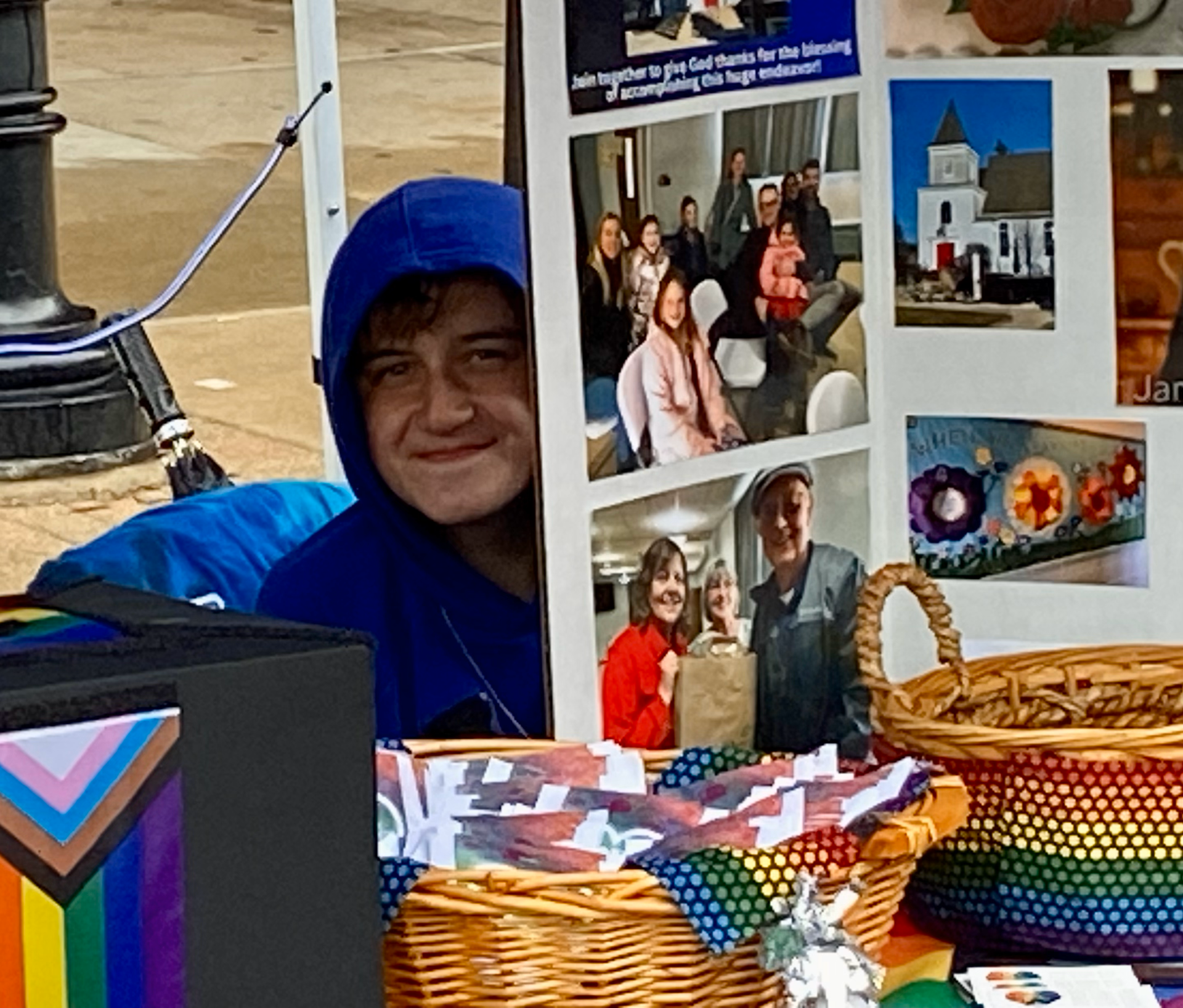 A man in a blue hoodie stands in front of a collage of pictures