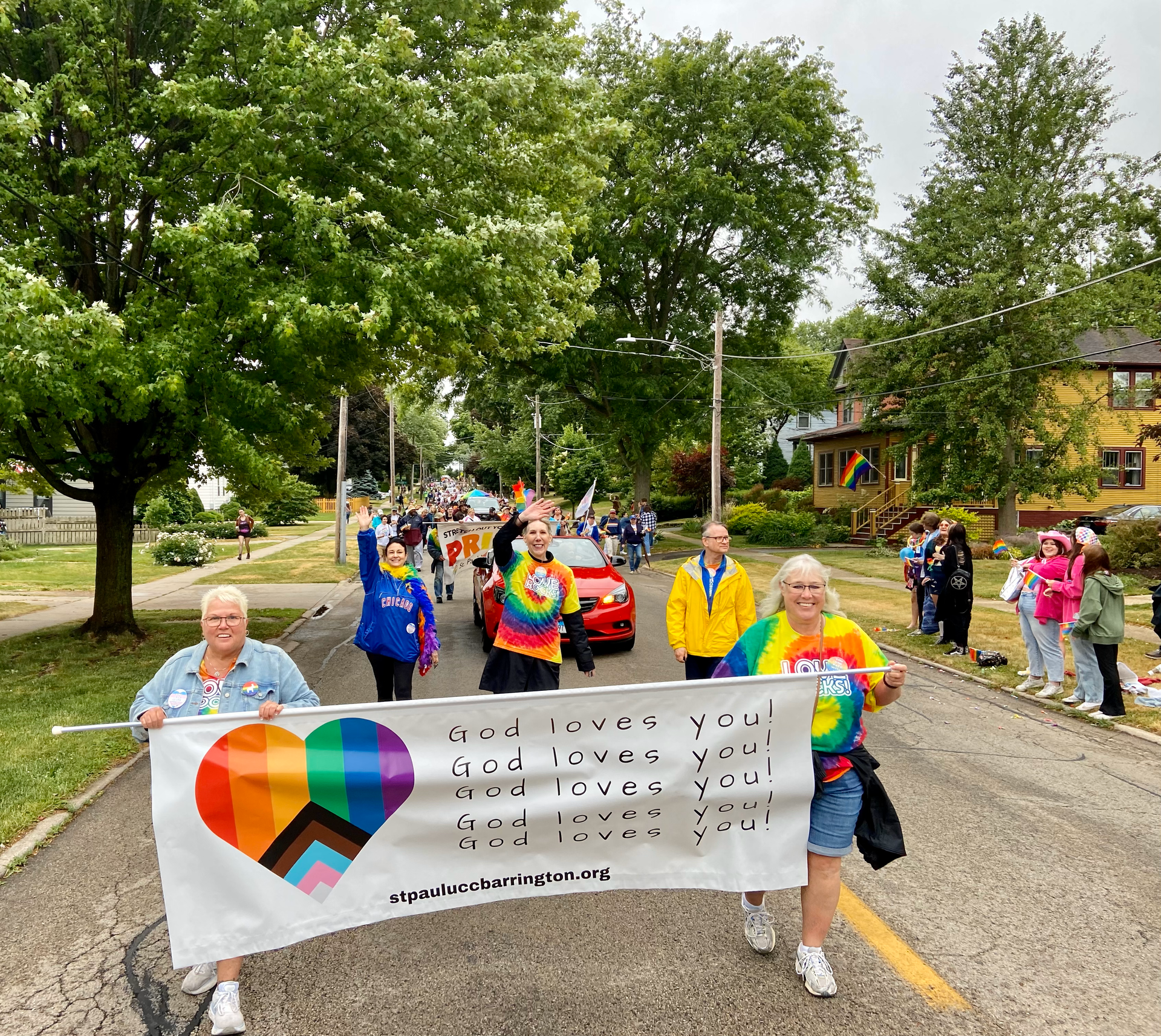 A group of people march down a street holding a banner that says god loves you