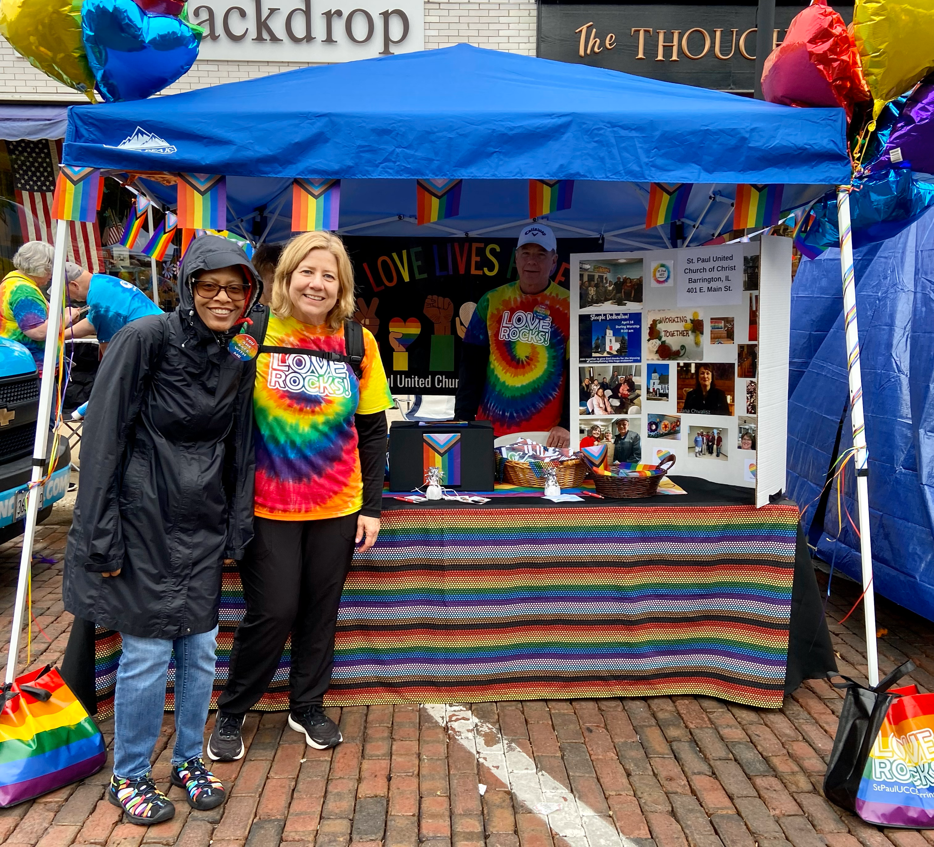 Two women are standing in front of a rainbow colored tent.