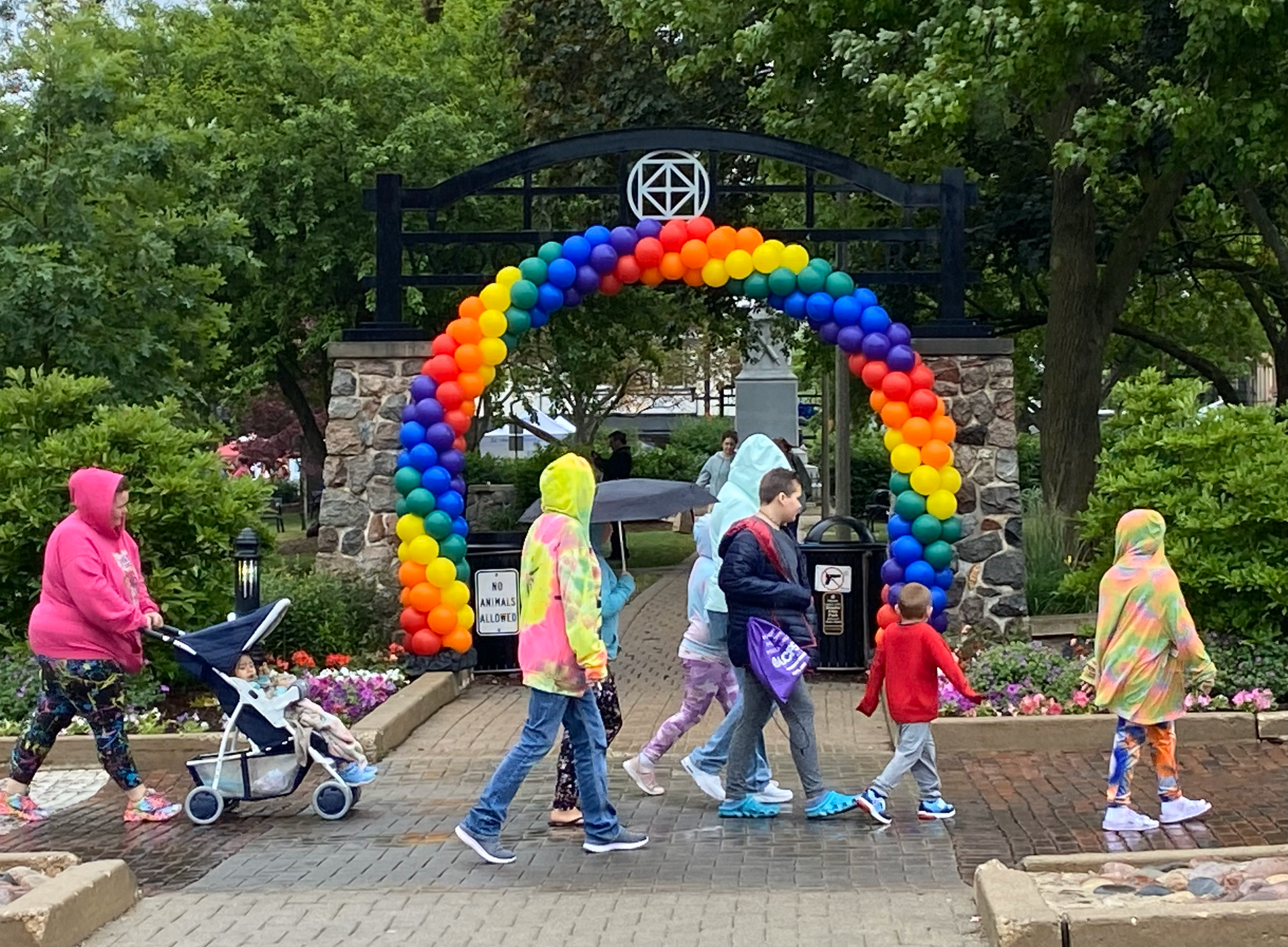 A group of people are walking under a rainbow balloon arch.