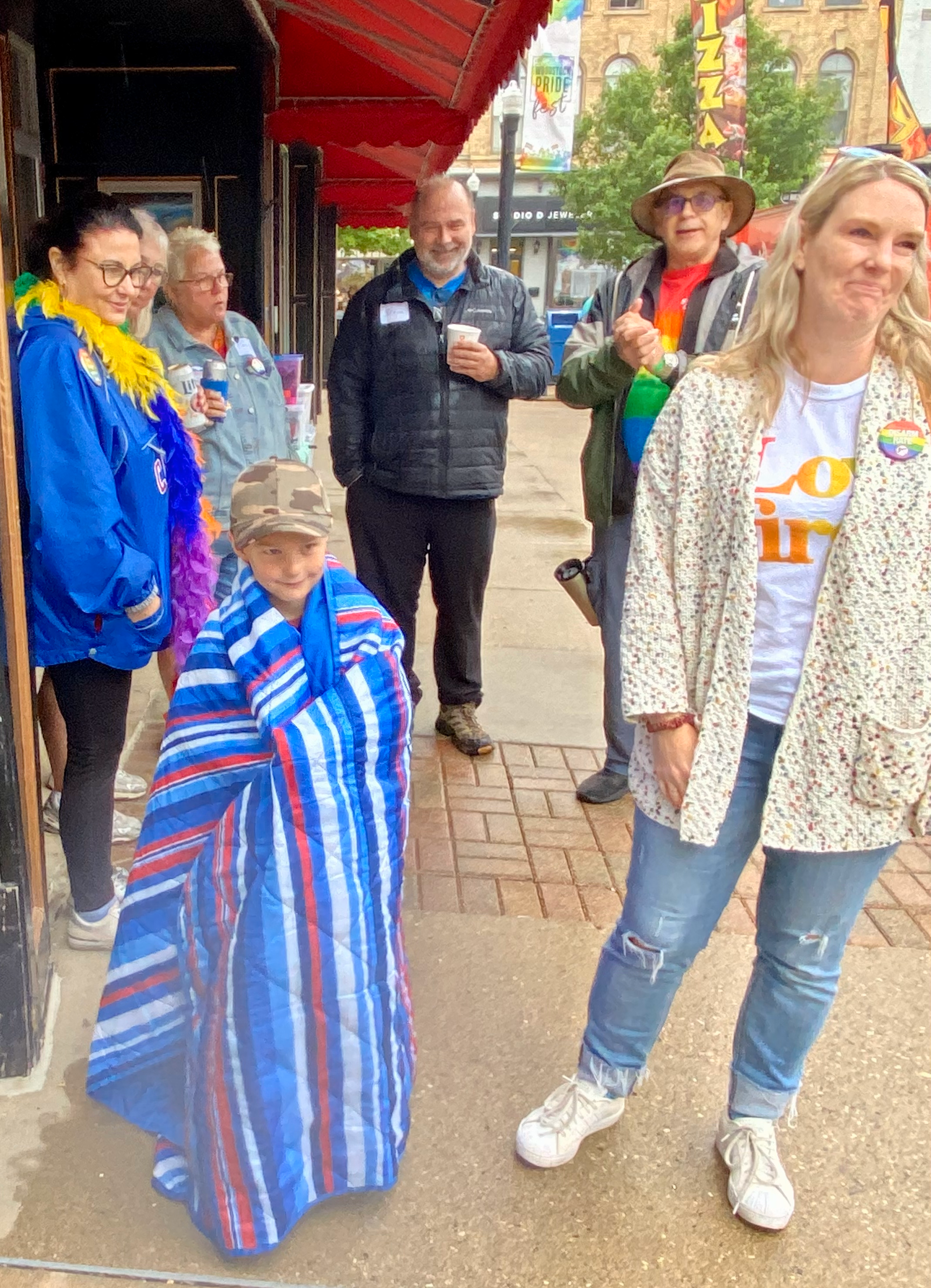 A group of people standing on a sidewalk wrapped in blankets.