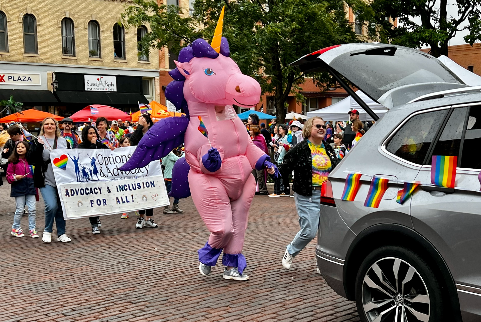 A person dressed as a pink unicorn is walking in a parade.