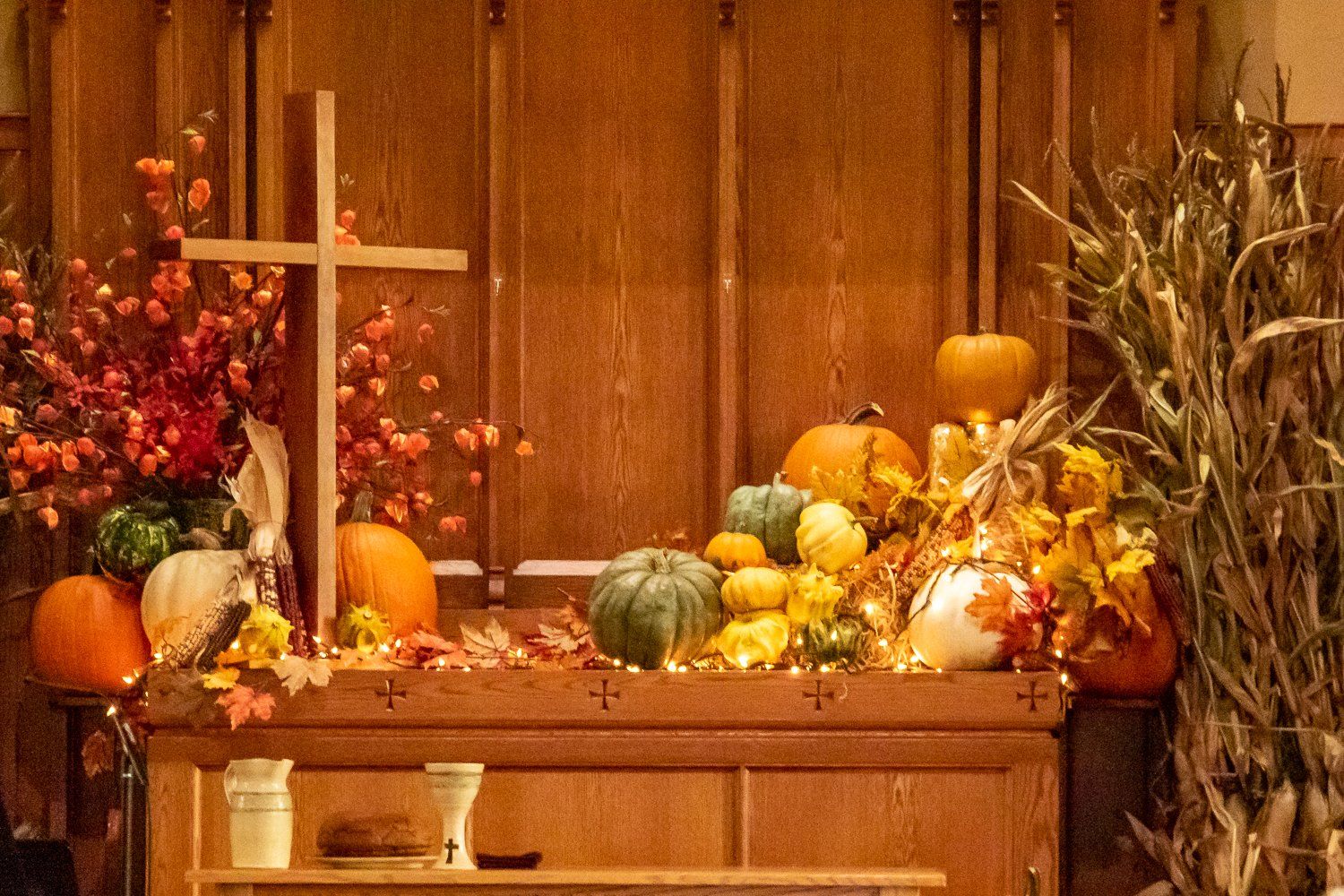 A church altar decorated for thanksgiving with pumpkins , leaves , and a cross.