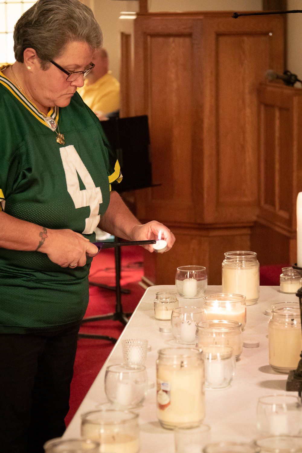 A woman in a green jersey is lighting a candle on a table.