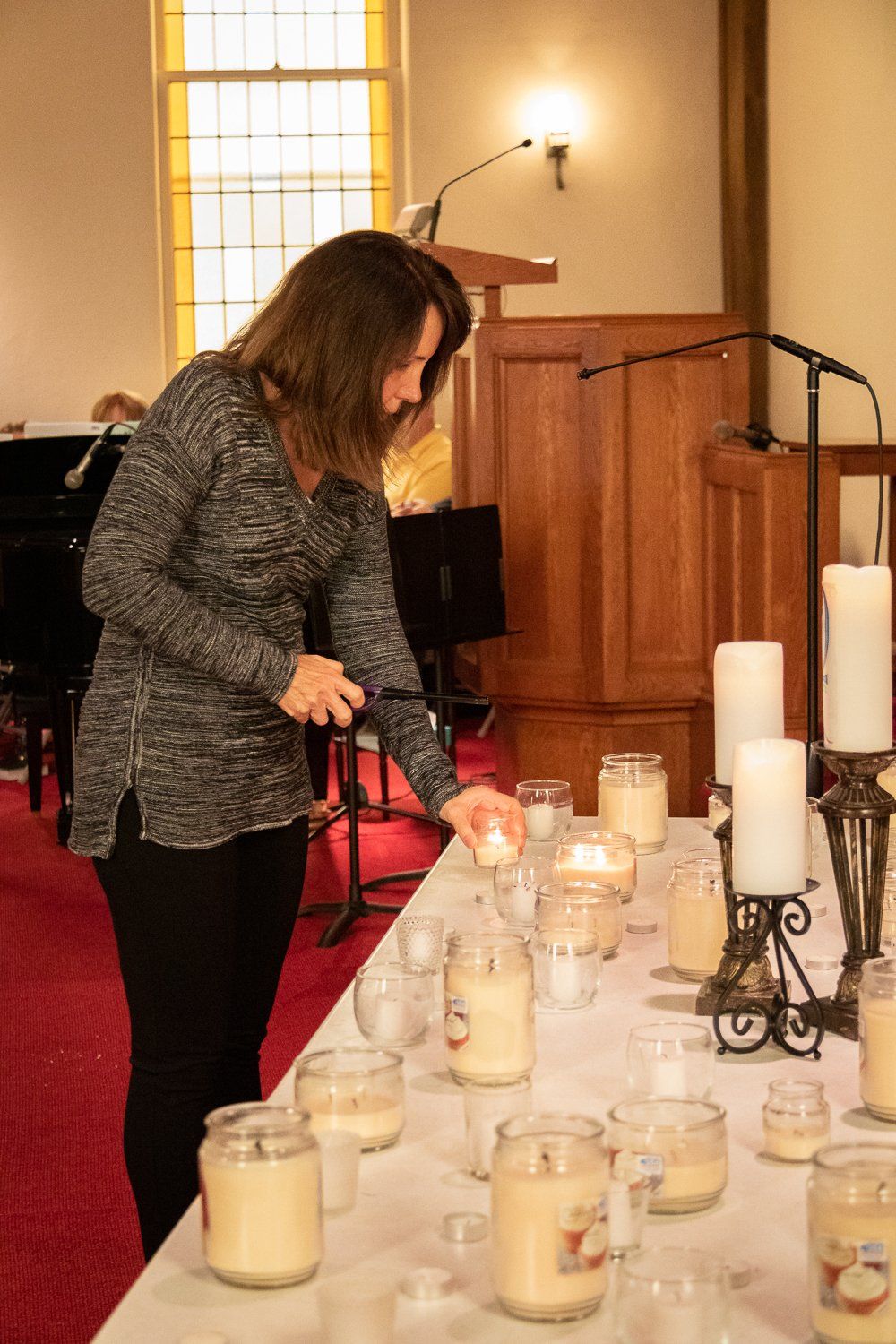 A woman is lighting candles on a table in a church.
