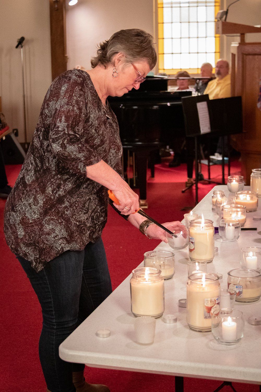 A woman is lighting candles on a table in a church.