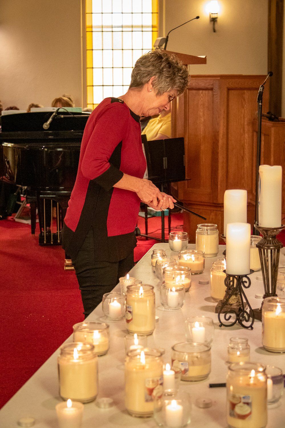 A woman is lighting candles on a table in a church.