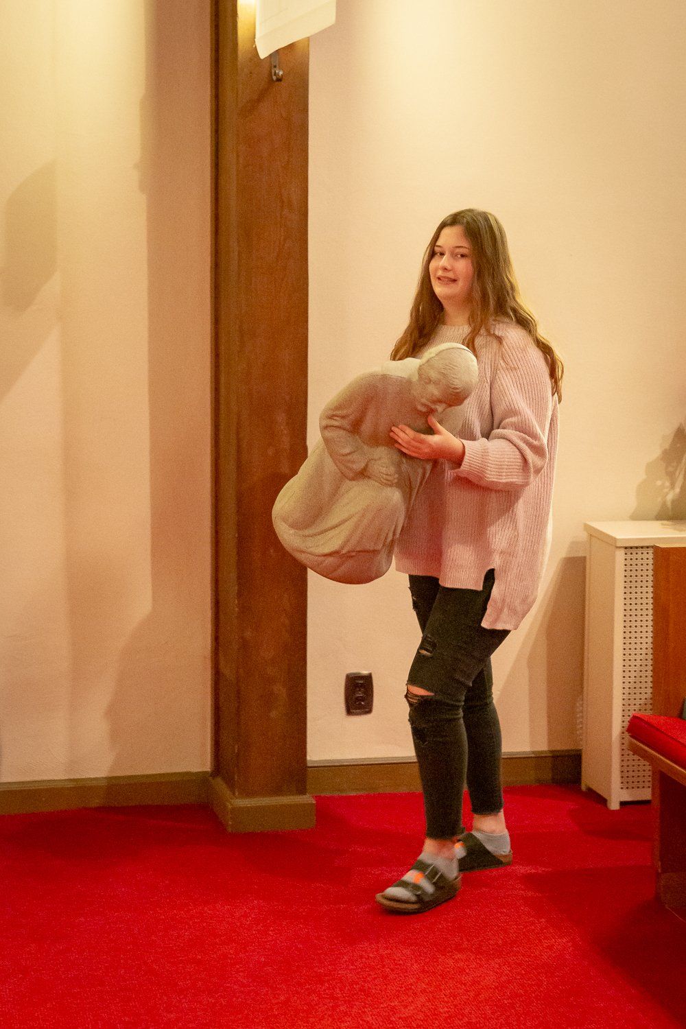 A young girl is standing on a red carpet holding a stuffed animal.