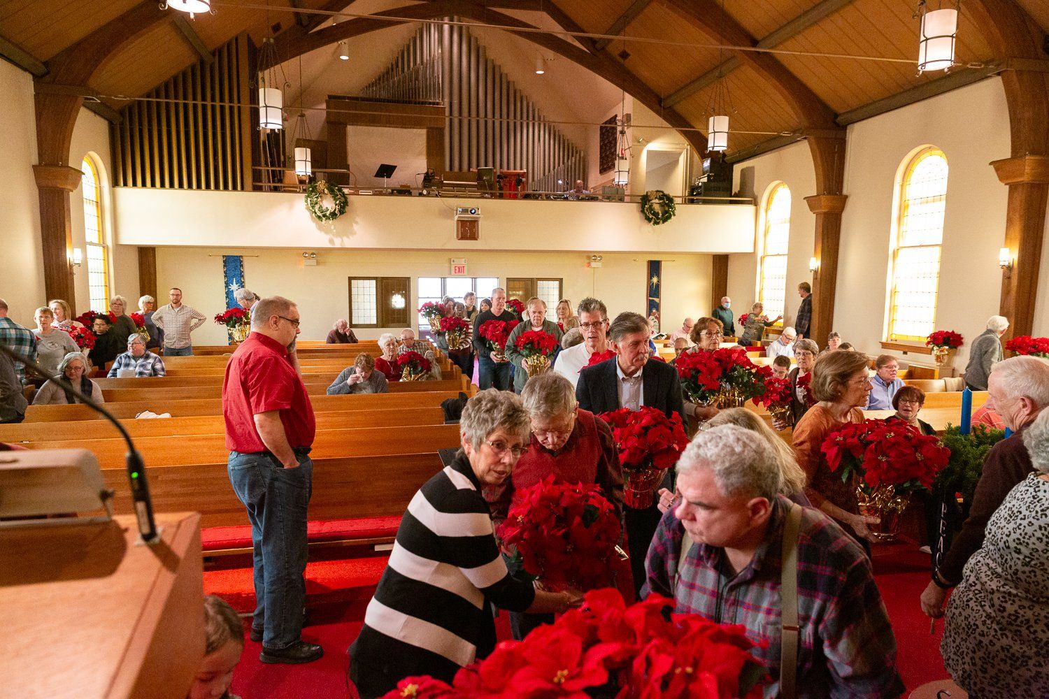 A group of people are standing in a church looking at red flowers.