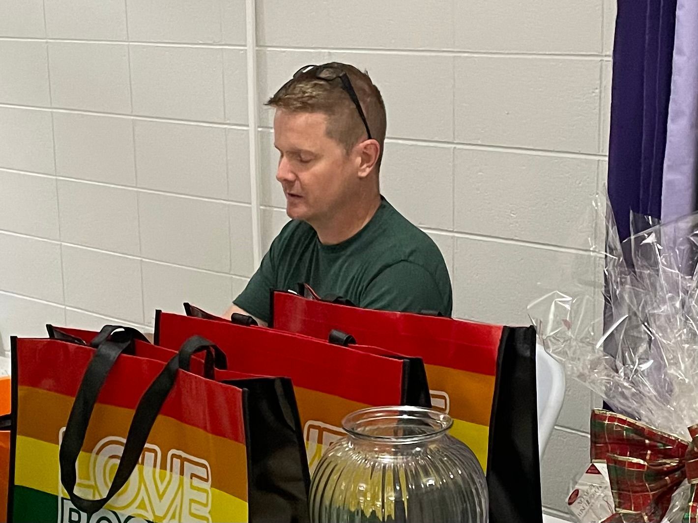 A man is sitting at a table surrounded by rainbow colored bags.