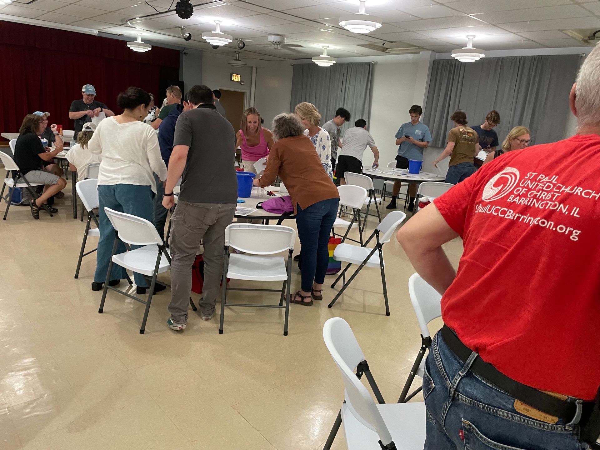 A group of people are standing around tables and chairs in a room.