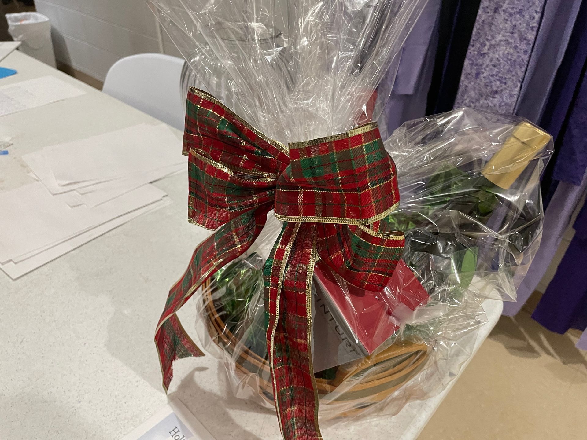 A gift basket wrapped in plastic with a bow on a table.
