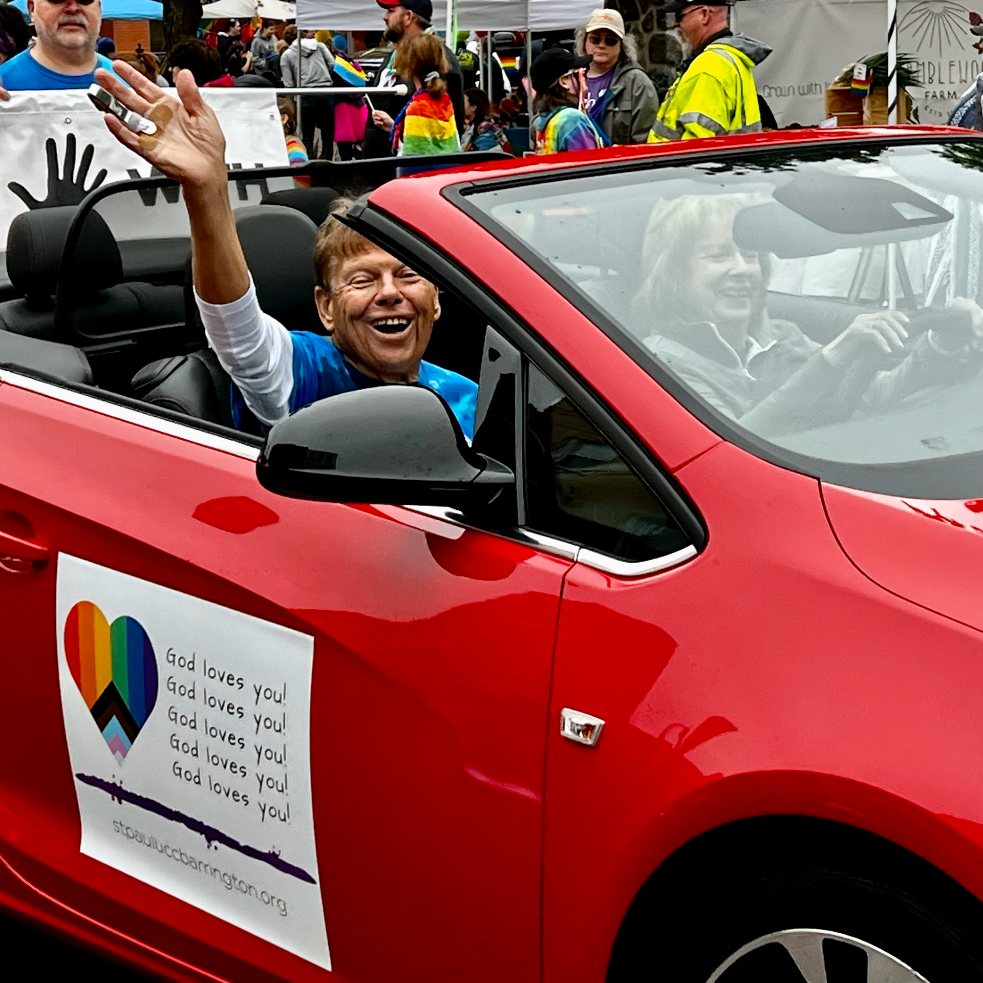 A red car with a sign on the side that says god loves you