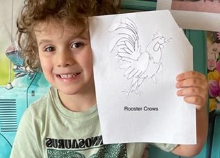 A young boy is holding up a drawing of a rooster.