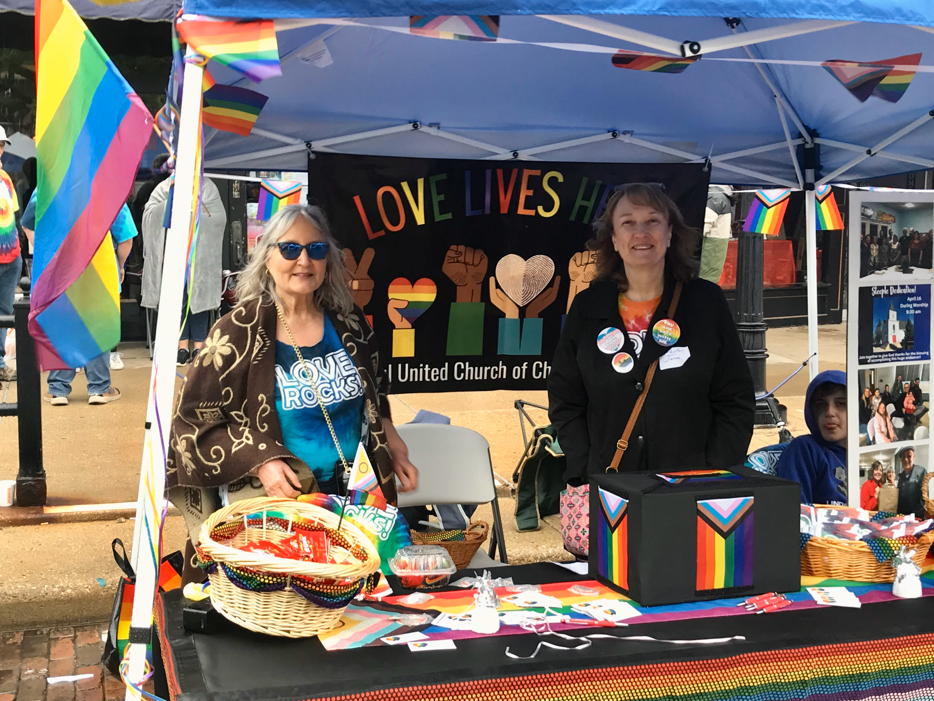 Two women are standing in front of a tent that says `` love lives ''.