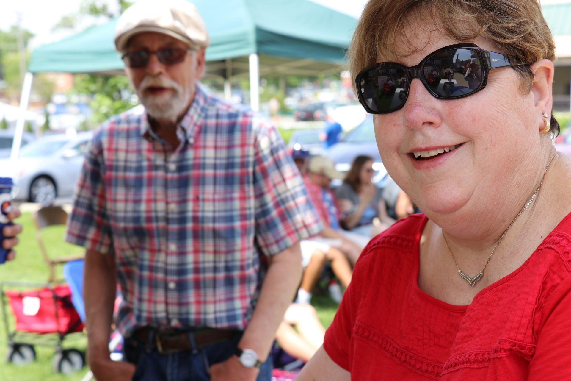 A woman wearing sunglasses is smiling in front of a man in a plaid shirt.